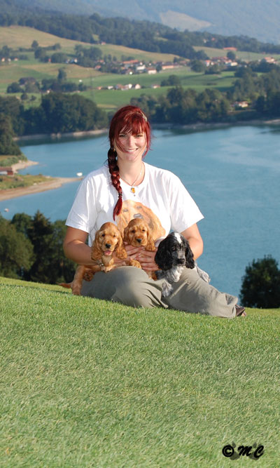 photo de Nadine Thomas sur le golf de Pont-la-Ville, tenant trois chiots cockers spaniels anglais issus de l'élevage de Syringa dans les bras, avec le lac de la Gruyère en arrière-plan.